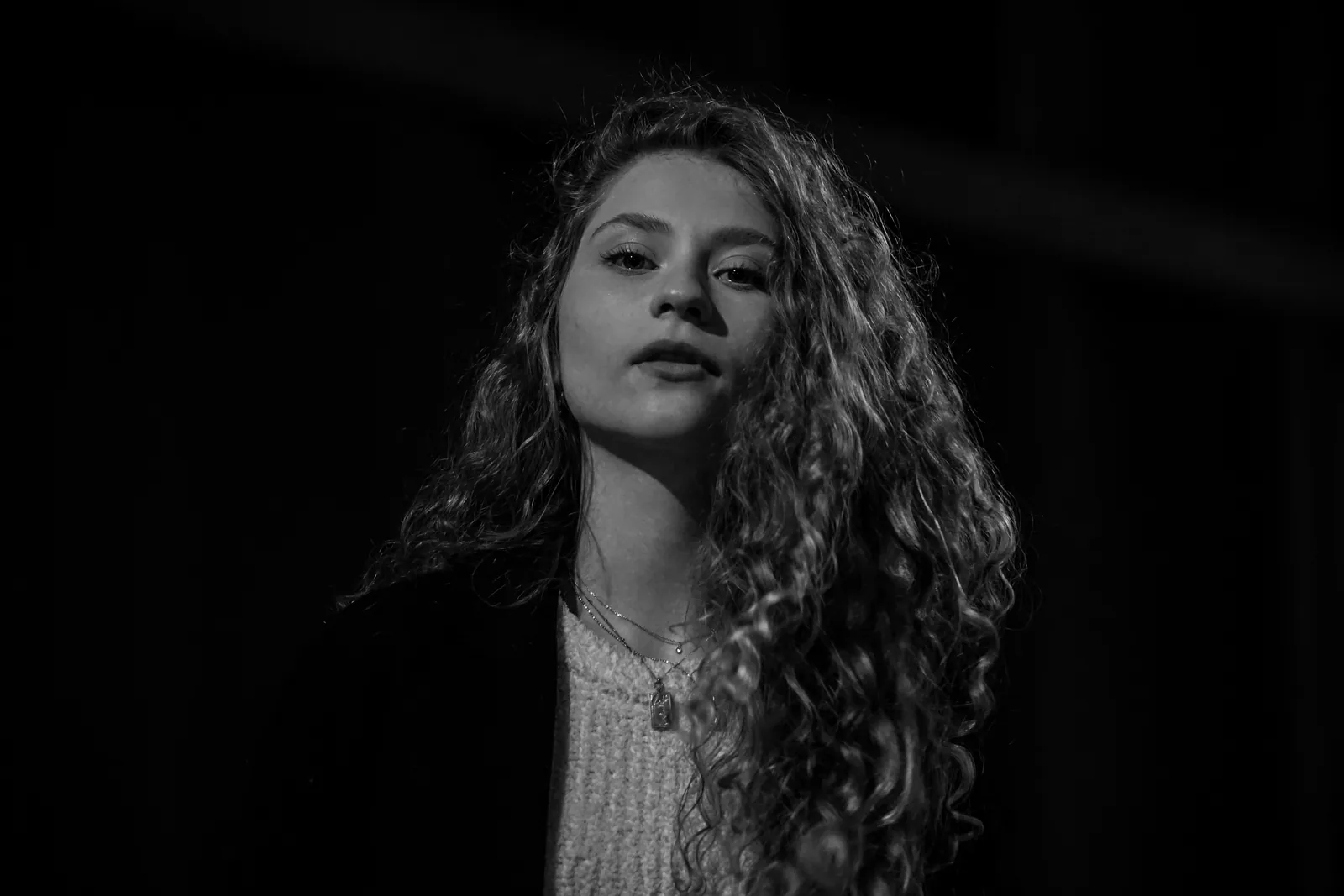 Czarno-biały portret kobiety o kręconych włosach na ciemnym tle